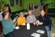 Zaproszeni goście siedzą przy stoliku, przeglądają broszurę z wystawy i piją herbatę