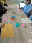 Grupa dzieci przy stole za pomocą modeliny i foremek odbija różne wzory i układa na kartce papieru