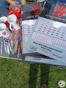 Zdjęcie przedstawia artykuły promocyjne: kubki, kalendarze, smycze, breloczki, długopisy, opaski odblaskowe dotyczące przeciwdziałaniu przemocy domowej