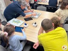 Nauczycielka prowadząca zajęcia wyciąga z pudełka i pokazuje inne karty gry do nauki programowania Scottie Go!