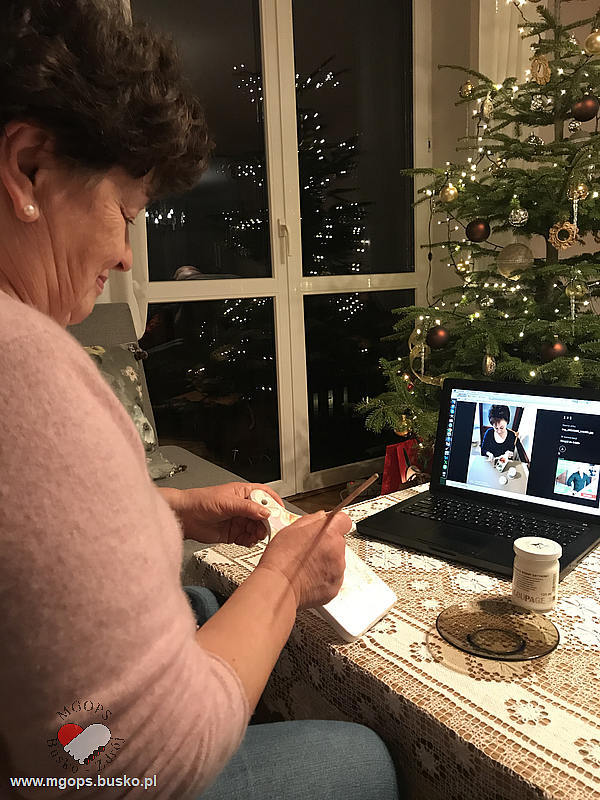 Seniorka łączy się przez komputer z instruktorką zajęć rękodzielniczych i wykonuje ozdobną deseczkę