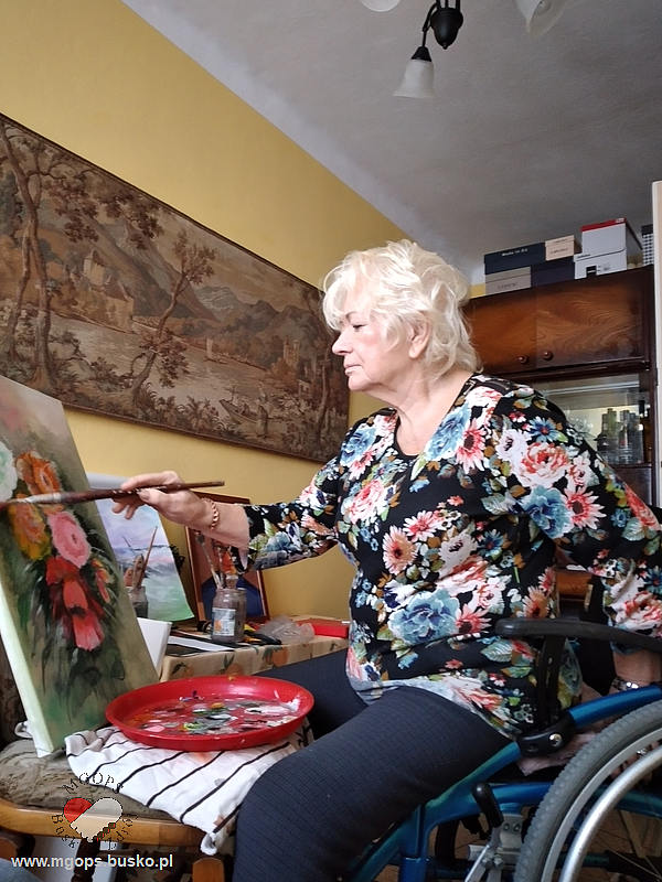Seniorka maluje obraz przedstawiający motyw kwiatowy